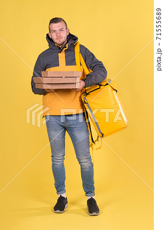 Food delivery smiling Caucasian young man in yellow jacket and with thermos bag on his shoulders on yellow background. Concept of Express food delivery in city, banner with space for text and slogan 71555689