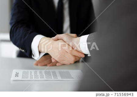Unknown businessman shaking hands with his colleague or partner above the glass desk in modern office, close-up. Business people group at meeting 71556943