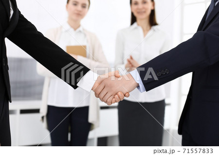 Businessman and woman shaking hands with colleagues at the background. Handshake at meeting in office. Concept of success in business 71557833