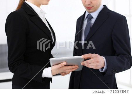 Businessman and woman using tablet computer for discussing questions in office. Partners or colleagues at meeting. Business cooperation concept Businessman and woman using tablet computer for discussing questions in office. Partners or colleagues at meeting. Business cooperation concept 71557847