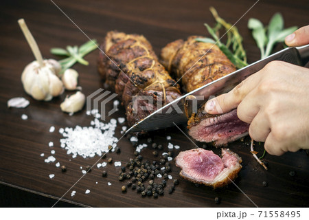 slicing organic roast beef roll on wood table with ingredients 71558495