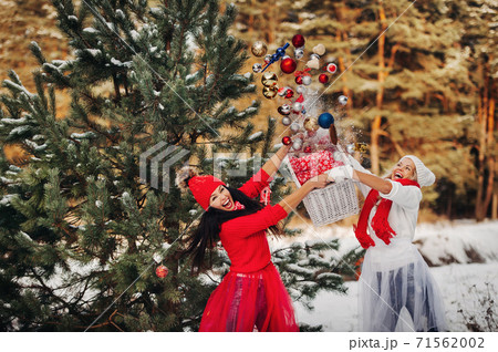 two girls near the Christmas tree throw a lot of toys on the tree. Christmas tree decoration on the street in winter.Lots of Christmas balls on the tree 71562002