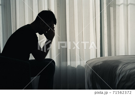 Silhouette depressed man sadly sitting on the bed in the bedroom, depression concept 71562372