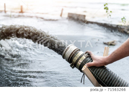 Engeneer hold pipe of power pump machine pouring mud sludge waste water with sand silt on ground. Sand-wash and coast-depeening. Septic sewage maintenance service. Industrial environment pollution 71563266