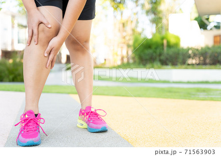 Female fatty runner athlete leg injury and pain. Hands grab painful knee while running in the park. Female fatty runner athlete leg injury and pain. Hands grab painful knee while running in the park. 71563903