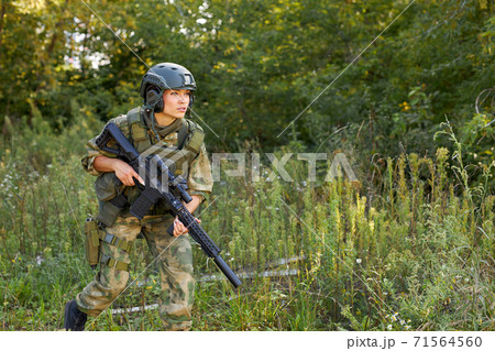 attractive brave military woman with a gun in forest, survival in wild forest 71564560