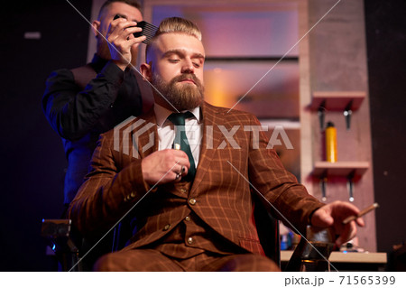 hairstylist cutting hair to business man smoking in salon 71565399