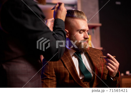 hairstylist cutting hair to business man smoking in salon 71565421