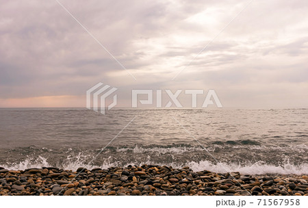 Rain clouds over the sea at sunset. Pebbles on the beach close-up, clouds colored the shades of pink and little waves on the water. 71567958