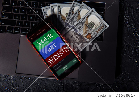 Smartphone with gambling mobile application and money banknotes on a keyboard. Sport and betting concept. Top view 71568617