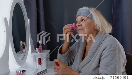 Old senior woman grandmother taking care of skin, applying anti-wrinkle foundation with sponge Old senior woman grandmother taking care of skin, applying anti-wrinkle foundation with sponge 71569491