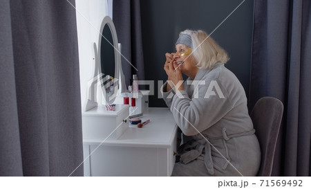 Old senior woman grandmother taking care of skin near eyes and wrinkles, putting makeup on at home Old senior woman grandmother taking care of skin near eyes and wrinkles, putting makeup on at home 71569492