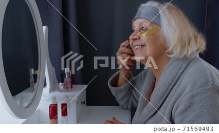 Old senior woman grandmother taking care of skin near eyes and wrinkles, putting makeup on at home Old senior woman grandmother taking care of skin near eyes and wrinkles, putting makeup on at home 71569493