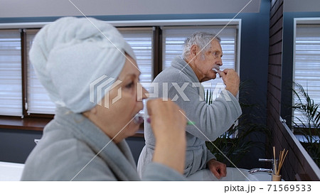 Senior couple grandmother and grandfather brushing teeth and looking into a mirror at bathroom 71569533