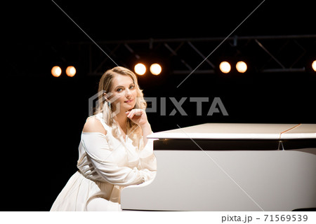 Pianist posing near white piano on the stage Pianist posing near white piano on the stage 71569539