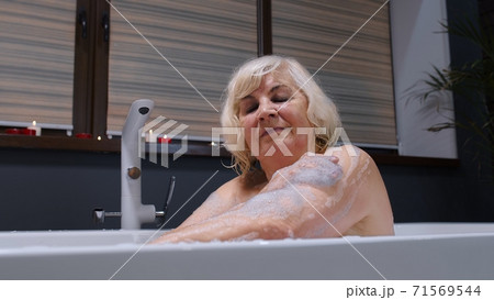 Beautiful active senior woman lying in warm bath with bubbles, enjoying relaxation. Elderly people Beautiful active senior woman lying in warm bath with bubbles, enjoying relaxation. Elderly people 71569544
