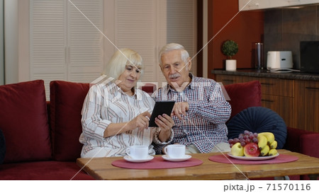 Senior old couple grandparents talking and using digital tablet computer at home. Internet shopping 71570116