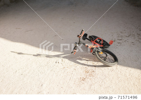Orange and black children's bicycle lying on the ground in a sandy park 71571496