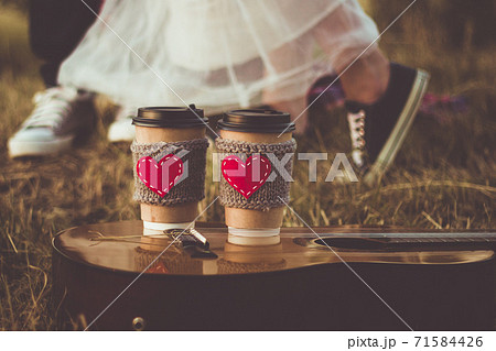 Romantic couple hugging while having picnic in sunset light. Coffee cup cozy knitted sleeve with felt red heart. 71584426