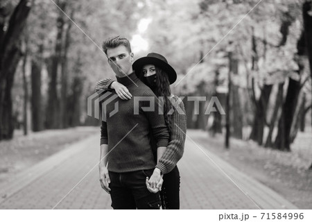 Young red haired woman puts on face mask while walking with young man in autumn park. Young red haired woman puts on face mask while walking with young man in autumn park. 71584996