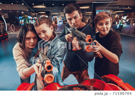 Mom helps daughter aim with toy gun in video game. Mom helps daughter aim with toy gun in video game. 71590704