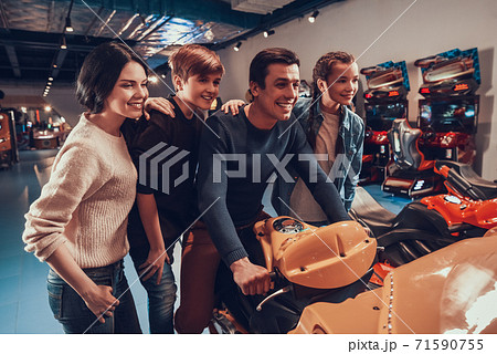 Dad sits on toy motorcycle while family is nearby Dad sits on toy motorcycle while family is nearby 71590755