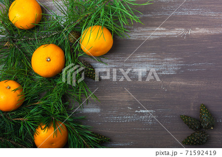Tangerines with fir and pine branches and cones on a brown wood background. Postcard for Christmas and New Year. Top view Tangerines with fir and pine branches and cones on a brown wood background. Postcard for Christmas and New Year. Top view 71592419