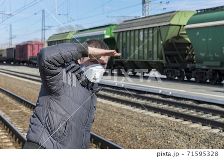 Man at the railway station waiting for his train, covering his face with his hand from the sun 71595328