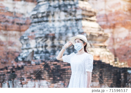 Tourist Woman in white dress wearing surgical face mask, protection COVID-19 pandemic during visiting in Wat Chaiwatthanaram temple in Ayutthaya. new normal, safety travel and Thailand travel concept Tourist Woman in white dress wearing surgical face mask, protection COVID-19 pandemic during visiting in Wat Chaiwatthanaram temple in Ayutthaya. new normal, safety travel and Thailand travel concept 71596537