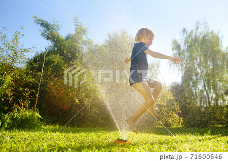 Funny little boy playing with garden sprinkler in sunny backyard. Funny little boy playing with garden sprinkler in sunny backyard. 71600646