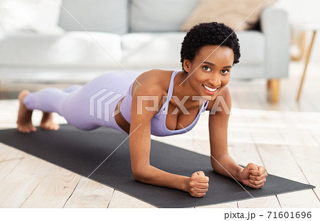 Full length portrait of smiling black woman in sportswear doing elbow plank on sports mat at home Full length portrait of smiling black woman in sportswear doing elbow plank on sports mat at home 71601696