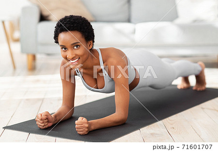 Muscle strengthening exercises. Happy African American woman doing elbow plank, training on yoga mat at home 71601707