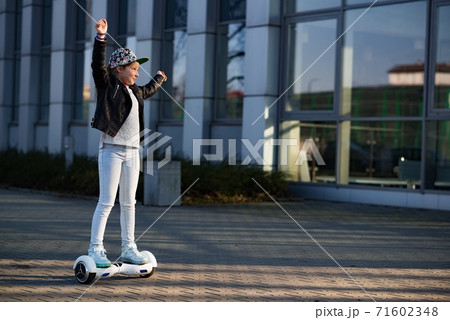 Happy and smiling young girl with hands up is riding on hoverboard. 71602348