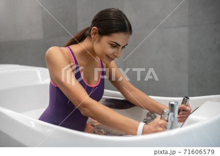 Dark-haired female sitting in hydromassage bathtub, receiving hydrotherapy 71606579