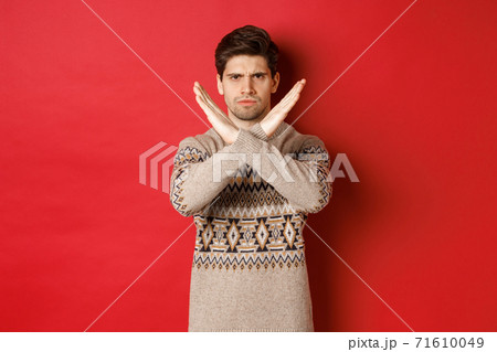 Image of angry and serious handsome man in christmas sweater, telling no or stop, showing cross gesture to restrict you from something, prohibit action, standing over red background Image of angry and serious handsome man in christmas sweater, telling no or stop, showing cross gesture to restrict you from something, prohibit action, standing over red background 71610049