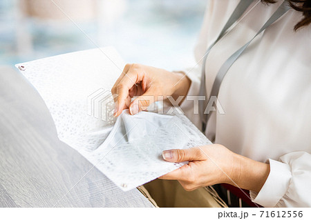 マスクケースに使用中のマスクを入れる女性の手元 71612556