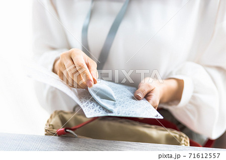 マスクケースに使用中のマスクを入れる女性の手元 71612557