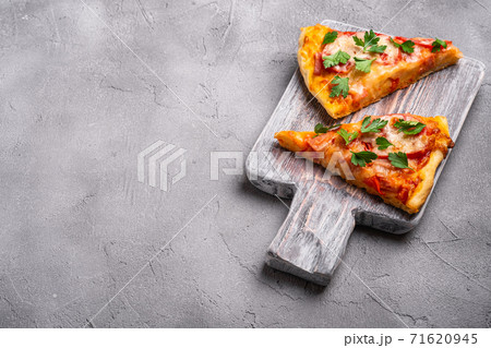 Hot pizza slices with mozzarella cheese, ham, tomato and parsley on wooden cutting board, stone concrete background, angle view copy space for text 71620945