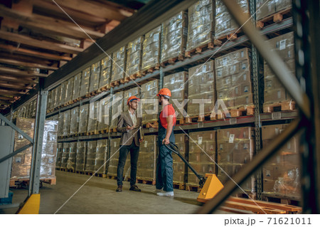 Manager in orange helmet talking to a warehouse worker 71621011