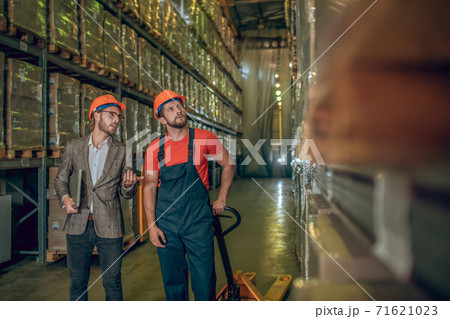 Manager inspecting warehouse while warehouse worker showing him the goods 71621023