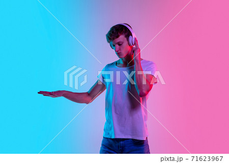 Young caucasian man's portrait on gradient blue-pink studio background in neon light 71623967