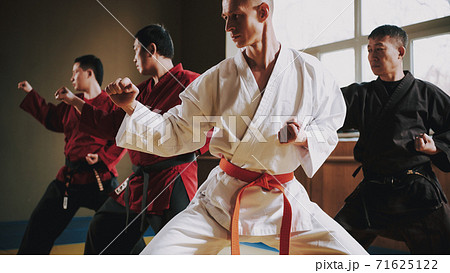 Man in a white kimono and red belt stands in rack. 71625122