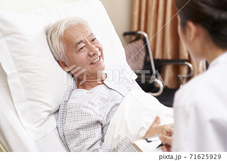 asian old man lying in bed talking to young female doctor in hospital ward 71625929