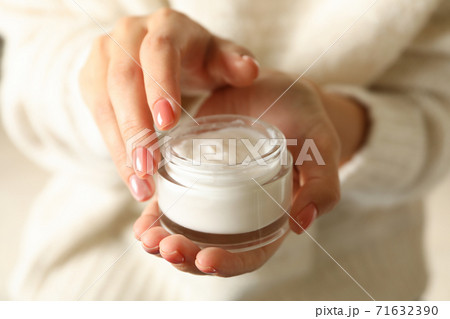 Woman in sweater with pink manicure hold jar of cosmetic cream 71632390