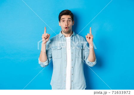 Portrait of amazed handsome man pointing fingers up, showing logo on blue background 71633972