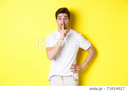 Image of excited guy planning surprise, shushing at camera, press finger to lip in hush sign, standing over yellow background 71634027