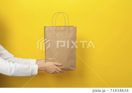 Female hands hold large gift bag made of brown craft paper on yellow background. Female hands hold large gift bag made of brown craft paper on yellow background. 71638626