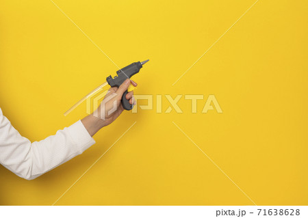 Female hand hold hot glue gun isolated on yellow background 71638628
