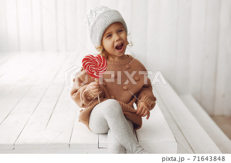Cute little girl sitting in a studio and eating candy Cute little girl sitting in a studio and eating candy 71643848