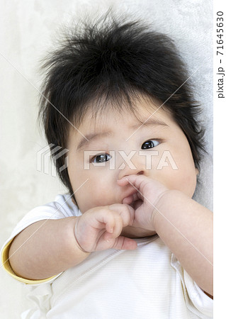 手を舐める赤ちゃんの顔 0歳 生後4か月 女の子 の写真素材